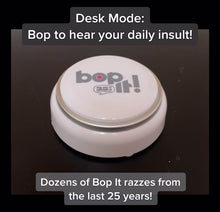 Load and play video in Gallery viewer, Bop it Button Demo - Bop it button on plain dark surface with hand pushing white and silver round button. It demonstrates desk mode where you get a daily insult and then Game mode where you can play Bop It on your own or with others.
