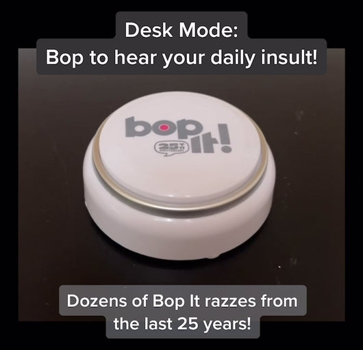Bop it Button Demo - Bop it button on plain dark surface with hand pushing white and silver round button. It demonstrates desk mode where you get a daily insult and then Game mode where you can play Bop It on your own or with others.